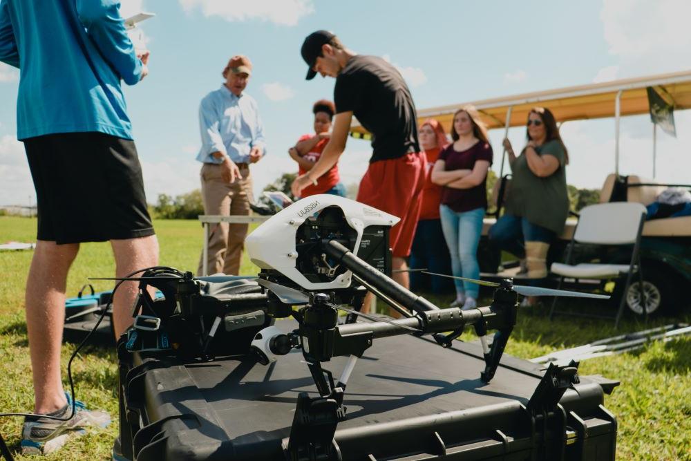 Aviation students working with a faculty member outside with drones over a green l和scape